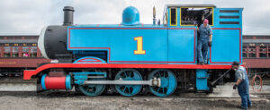 Two railroad engineers on and next to the Thomas the Tank Engine.