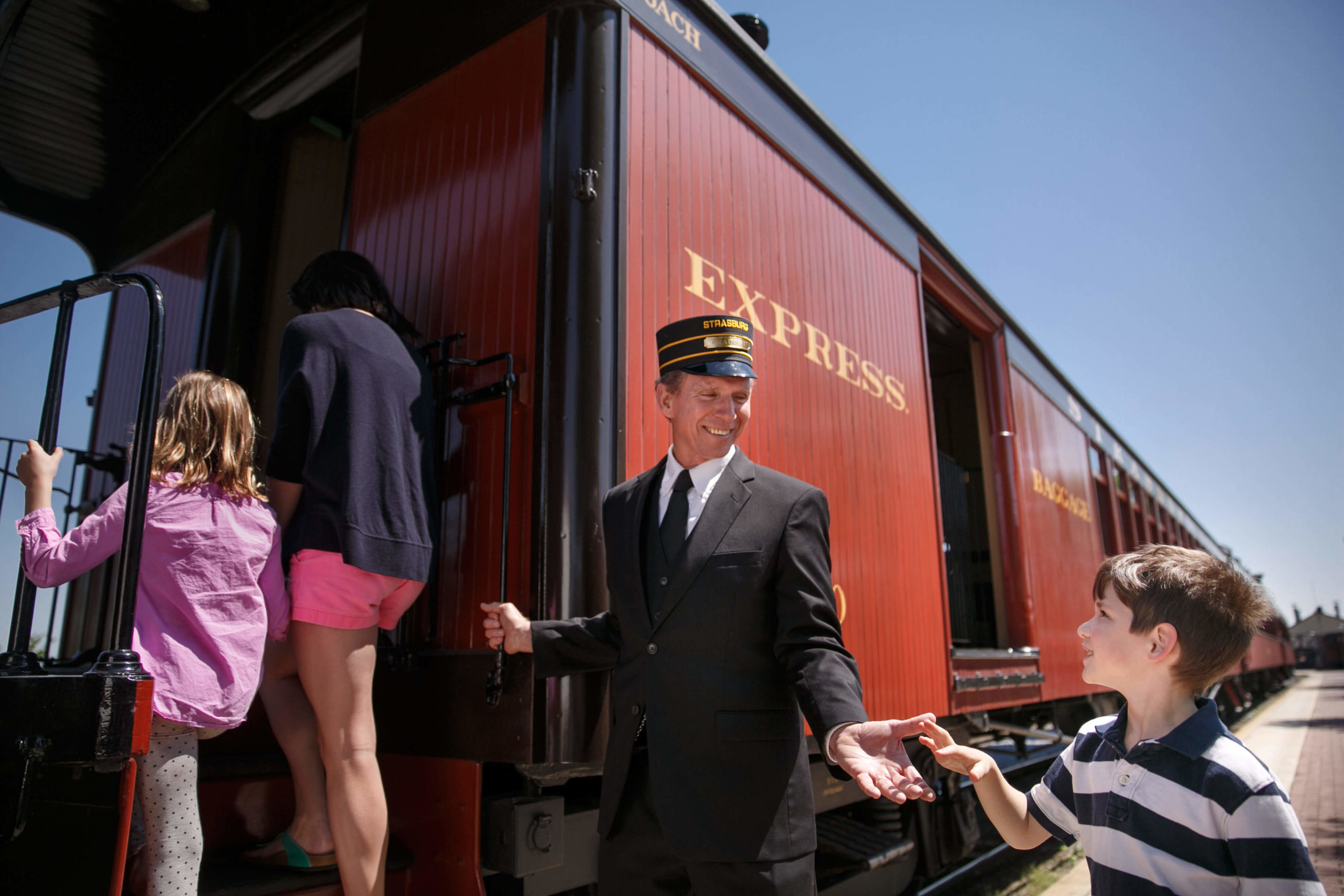 A group of children boarding a train at Strasburg Rail Road while a conductor helps them.
