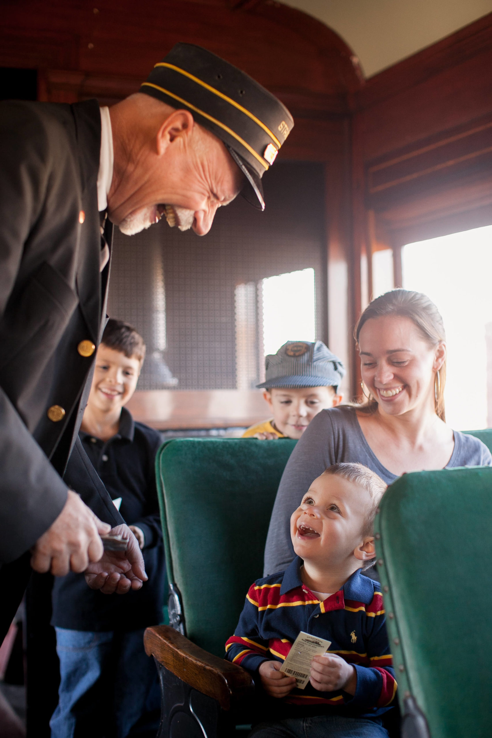 A little boy smiles at a train conductor while holding a train ticket.