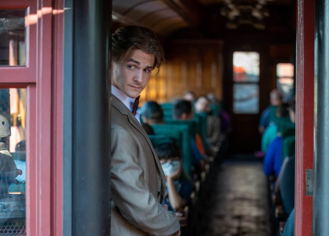 A performer for the murder mystery standing stealthily along an inside train door.