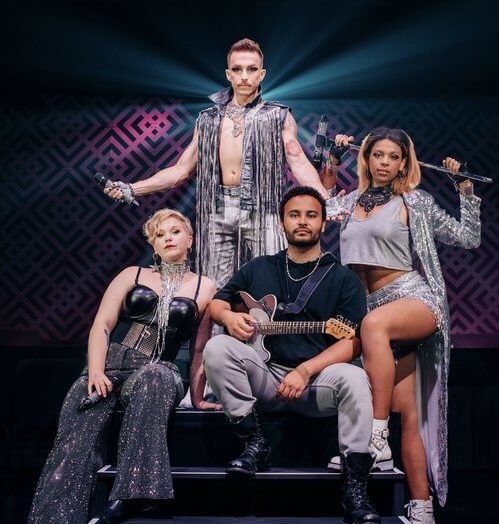 A group of performers on a stage posing for the camera with instruments and flashy outfits.