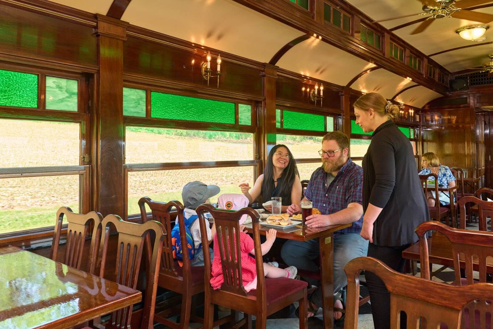 A family of four sitting at a table in a dining car on a passenger train while the waitress checks on them.