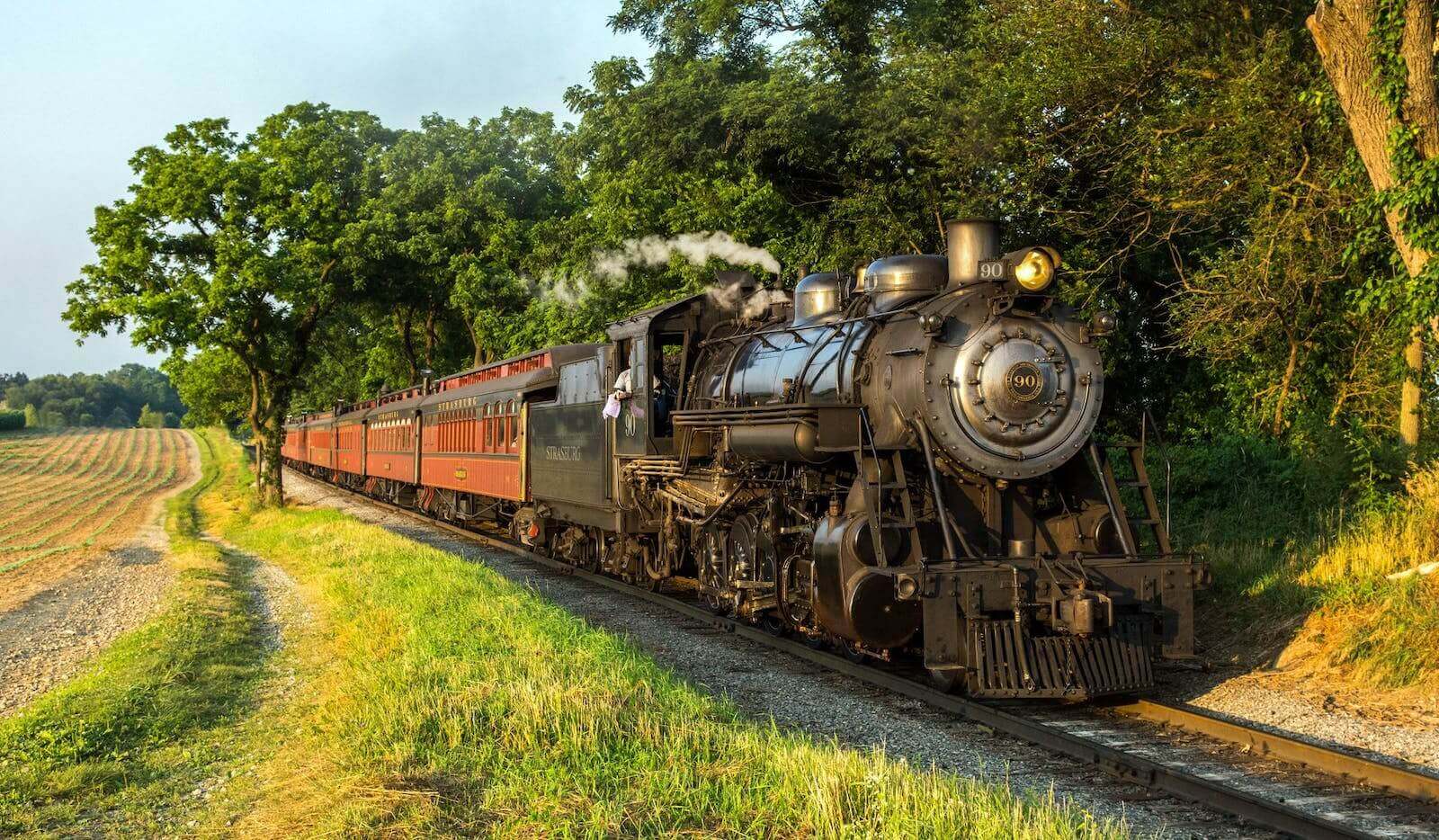 Steam engine 90 traveling down train tracks near a forest.