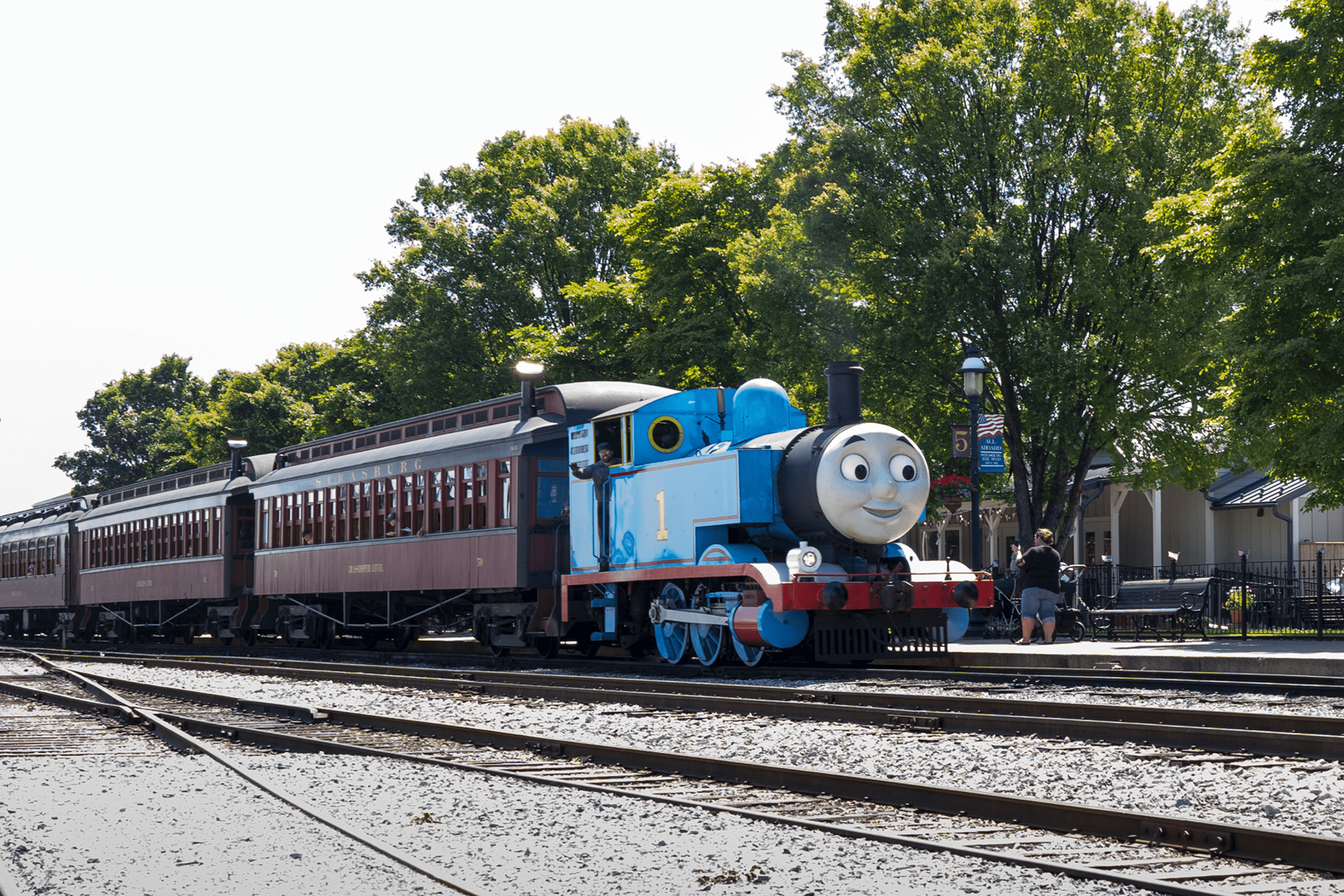 Thomas the train traveling on train tracks with train cars attached to him.