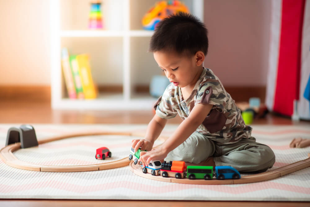 A little boy sitting on the floor playing with wooden trains.
