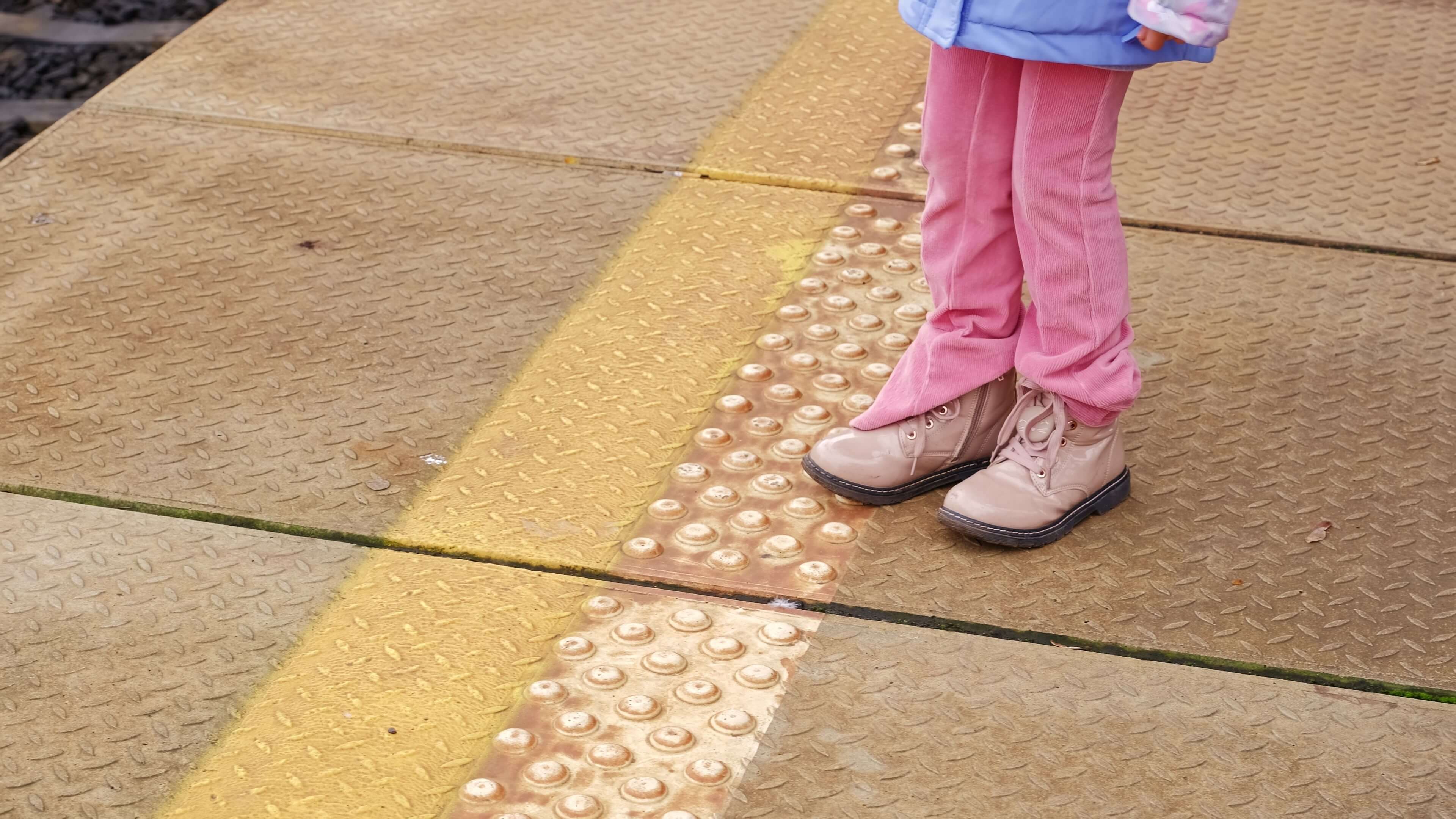 a little girl standing at the edge of the yellow safety lines at a railroad station
