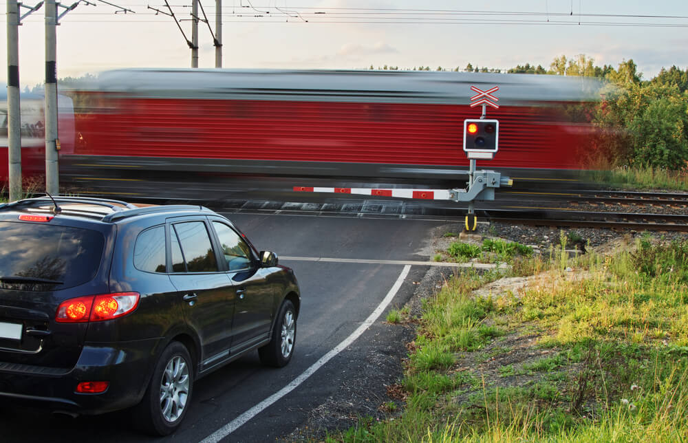 car sitting at a railroad crossing as a train passes by