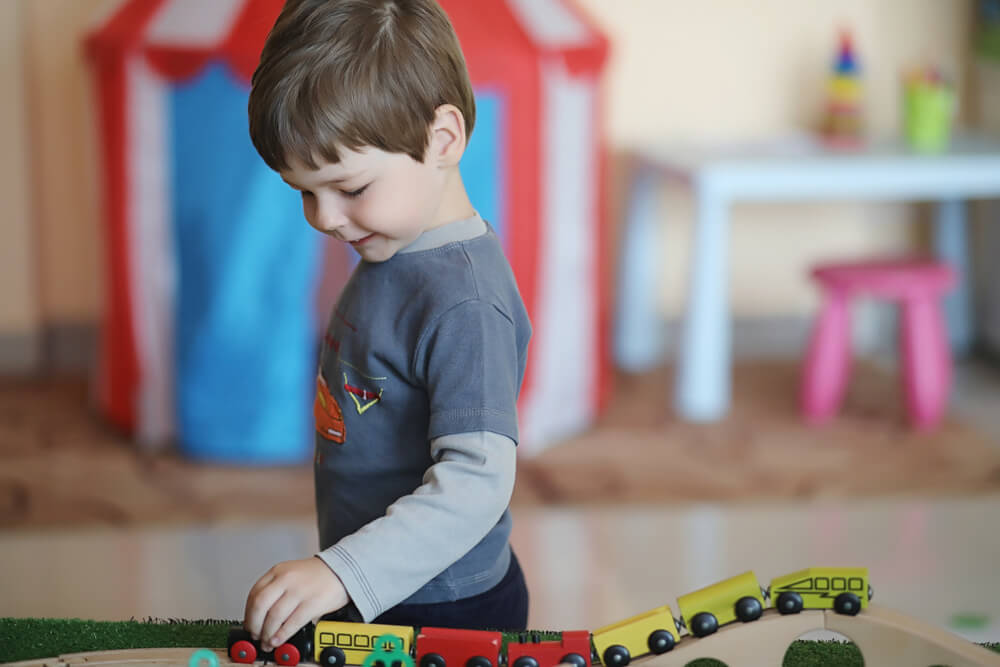a little boy playing with wooden trains on a wooden train track