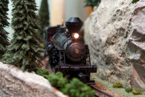 A close up of a model train running on a track in the middle of a forest and a mountain.