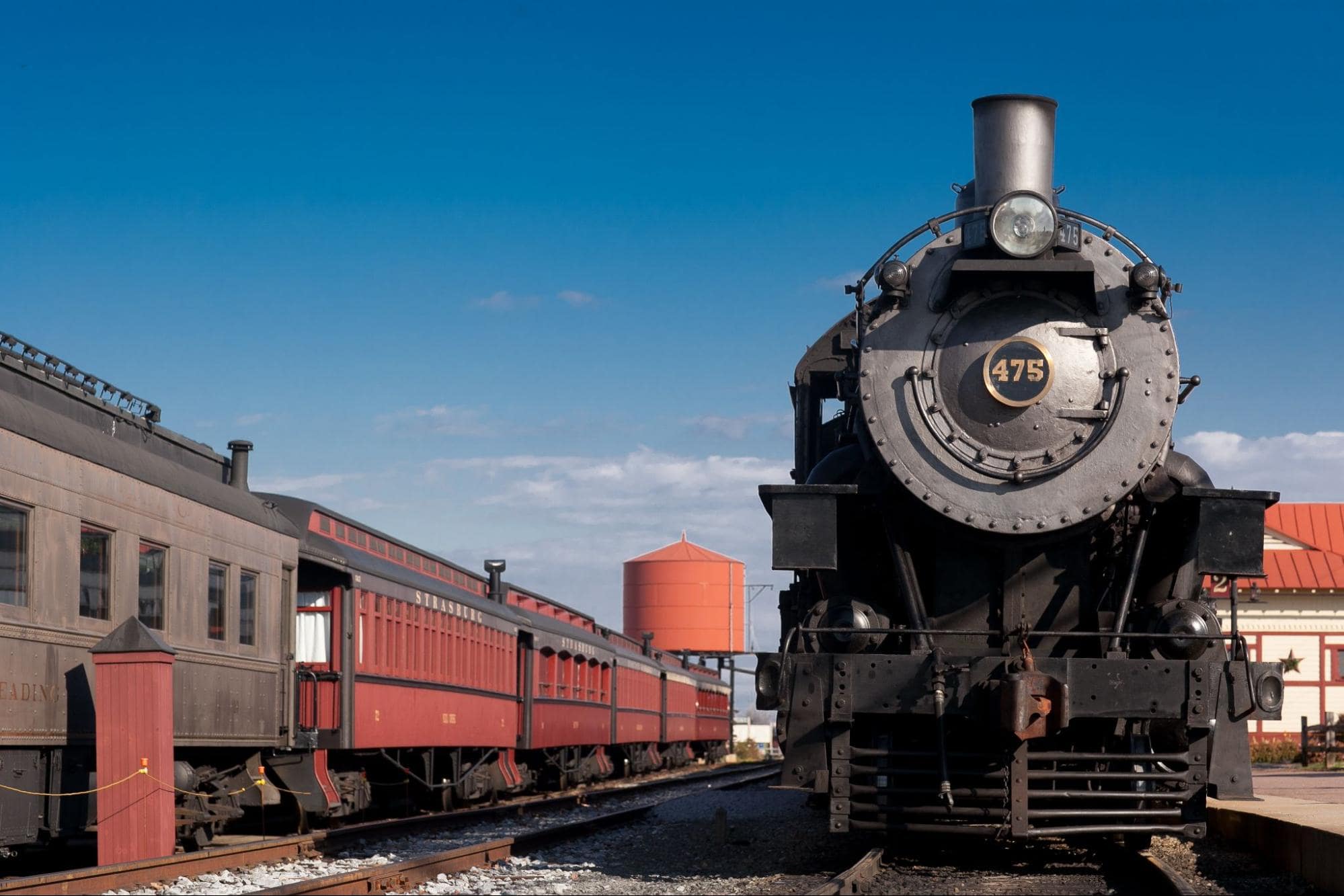 Railroad photography of a black steam locomotive numbered 475 at a train station with blue sky.