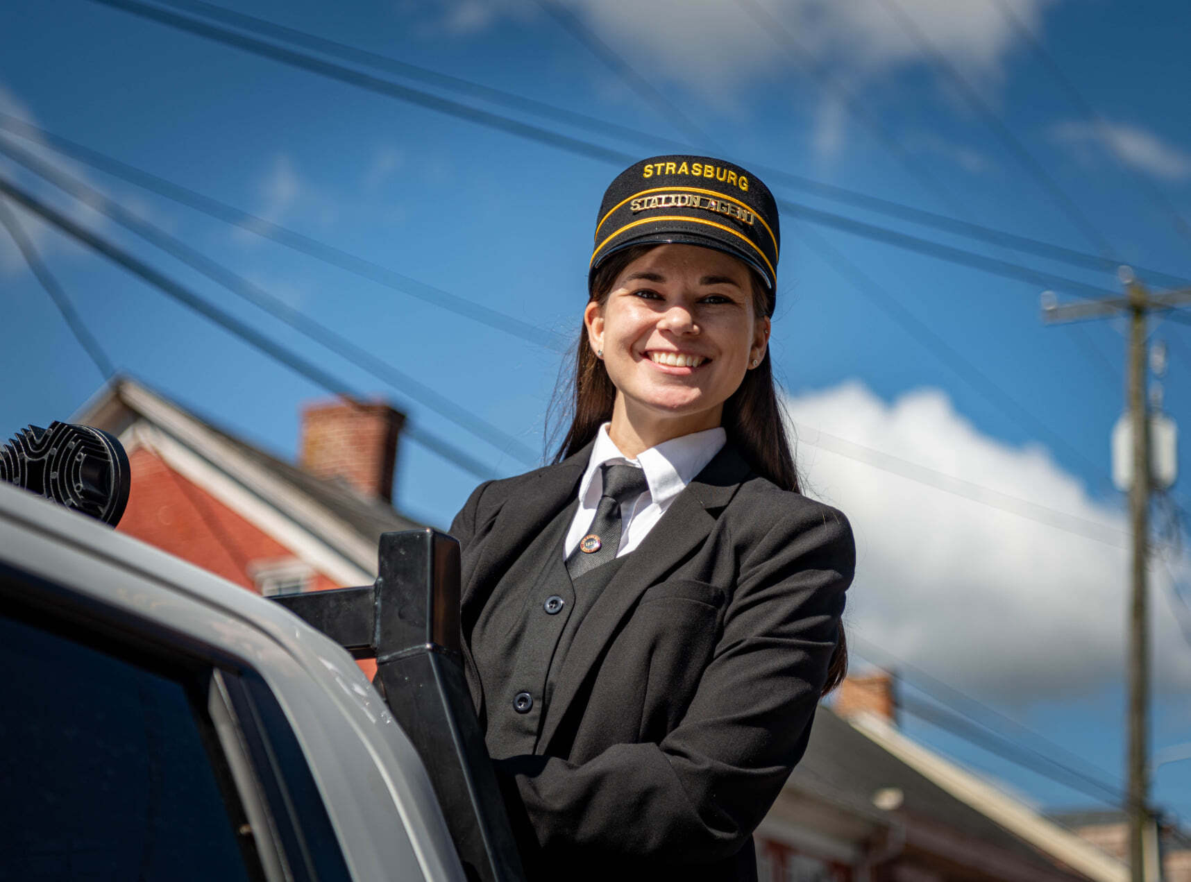 Smiling railroad woman from Strasburg Railroad in a train conductor uniform and cap outside with blue sky background.